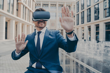 Excited office worker in VR glasses, checking info in cyberspace, sitting on bench outdoors. Happy...