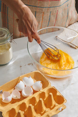 top view of woman beating eggs for an omelette or pie. Cook delicious and healthy food at home for breakfast. A whisk or mixer for convenience of cooking protein dish. broken eggshells and paper box