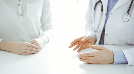 Doctor and patient discussing current health questions while sitting near of each other at the table in clinic, just hands closeup. Medicine concept