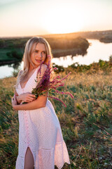 Portrait of a blonde young woman with wildflowers on nature background in summer at sunset. female is relaxing in the field with flowers. Soft golden color