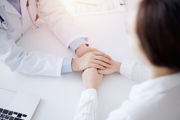 Obraz na płótnie Canvas Doctor and patient sitting opposite each other at the table in clinic office. The focus is on female physician's hands reassuring woman, only hands, close up. Medicine concept