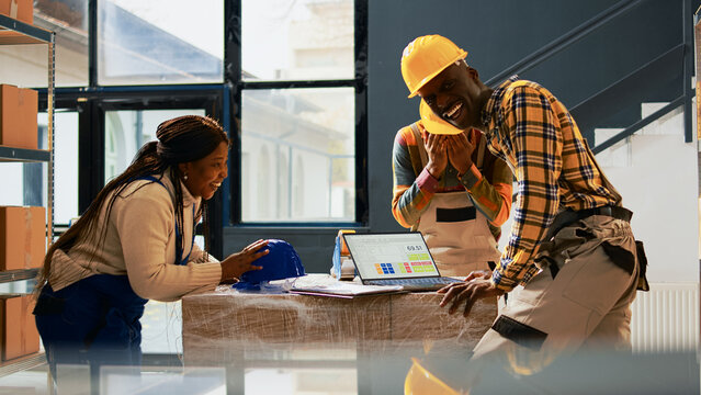 Happy employees working on packing goods in depot, making jokes before planning logistics with lists and laptop. Team of people putting merchandise in containers, quality control.