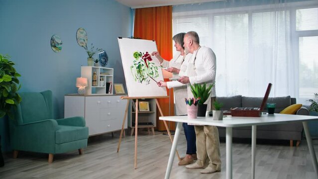 retired entertainment, talented elderly man and woman paint modern picture on canvas with brushes and paints at home