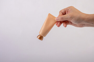 Female hand holds cosmetic product in tube, bottle, lotion or serum on white background.