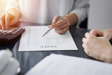 Woman accountant using a calculator and laptop computer while counting taxes for a client. Business...