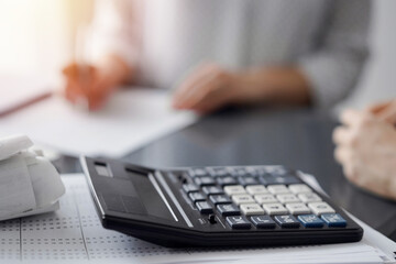 Woman accountant using a pen and laptop computer while counting and discussing taxes with a client, focus on the calculator. Business audit and finance concepts