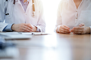 Doctor and patient discussing something while sitting near each other at the wooden desk in clinic. Medicine concept