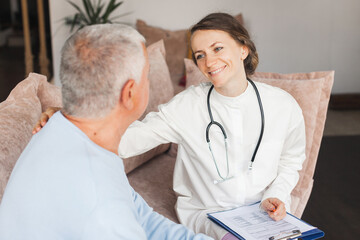 Female professional doctor showing medical test result explaining prescription using clipboard visiting senior elderly old man patient at home sitting on sofa