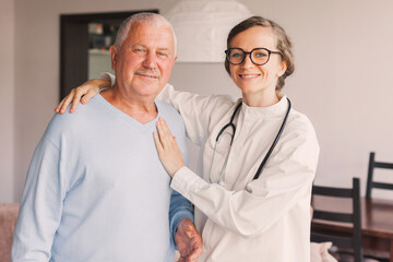 Female professional doctor showing medical test result explaining prescription using clipboard visiting senior elderly old man patient at home sitting on sofa