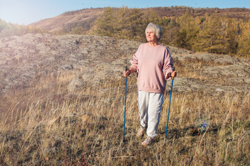 Attractive short haired middle aged woman in activewear hiking in forest using poles for nordic walking