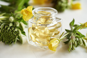 Gel capsules of evening primrose oil in a bottle with fresh plant