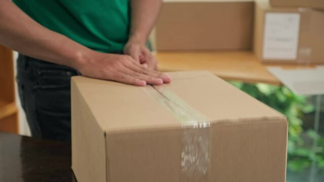 Close-up of man using sticky tape to pack box and outting postage stamp on it at office