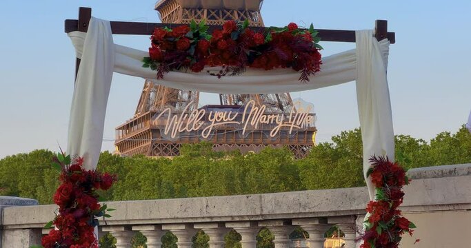 Arch with flowers in front of the Eiffel Tower in Paris. Establishing shot man making surprise proposal of marriage to his beloved woman near eiffel tower