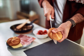 A close-up o a man slicing bread, and preparing to make a delicious sandwich.