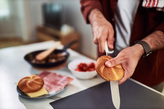 A man preparing sandwiches in the kitchen at home, slicing bread with a knife.