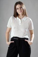 Beautiful young woman posing in a white polo shirt in photo studio	in front of grey background
