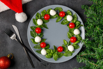 Caprese salad in the form of a Christmas wreath. Festive tomato mozzarella and basil appetizer on grey plate.