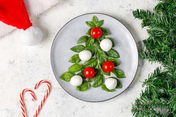 Caprese salad in the form of a Christmas tree. Festive tomato mozzarella and basil appetizer on light plate.