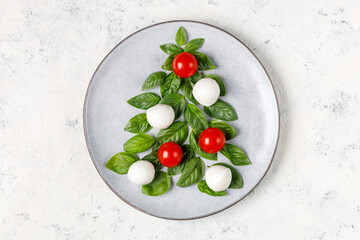 Caprese salad in the form of a Christmas tree. Festive tomato mozzarella and basil appetizer on light plate.