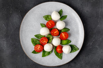 Caprese salad in the form of a Christmas tree. Festive tomato mozzarella and basil appetizer on light plate.