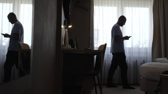 Static shot of caucasian middle-aged man pacing across dark room with phone