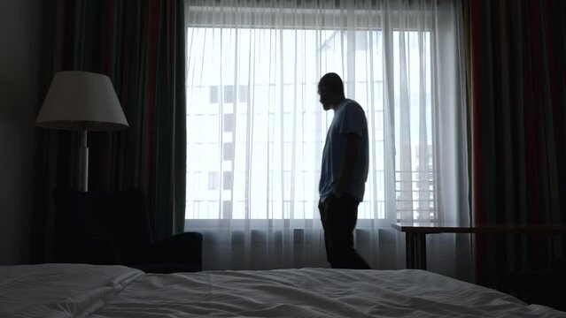 Medium shot of anxious middle-aged man pacing across dim hotel room
