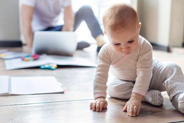 Baby daughter sitting on floor near father working at laptop