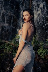 Obraz na płótnie Canvas Young woman in wet dress standing near waterfall.