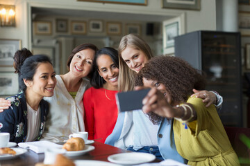 Smiling women friends taking selfie at restaurant table