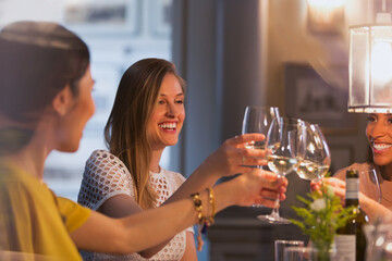 Smiling women friends toasting white wine glasses dining in restaurant