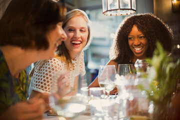 Laughing women friends talking and dining at restaurant table