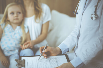 Doctor and patient. Pediatrician using clipboard while examining little girl with her mother at home. Sick and unhappy child at medical exam. Medicine concept