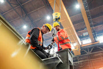 Steel workers fastening steel to crane in factory - obrazy, fototapety, plakaty