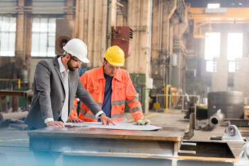 Manager and steel worker engineer reviewing blueprints in factory