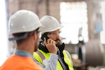 Steel workers talking on cell phone in factory - obrazy, fototapety, plakaty