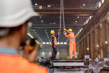 Steel workers adjusting crane hooks in factory