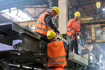 Steel workers fastening crane hook to steel in worker - obrazy, fototapety, plakaty