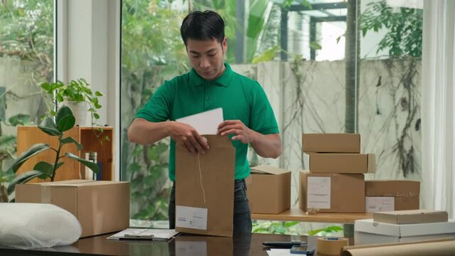 Medium shot of Mail worker in green uniform packing documents in envelope to ship customers at office