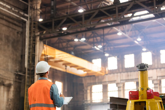 Steel worker with clipboard looking up in factory