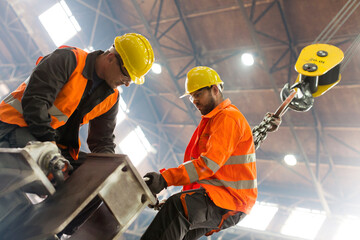 Steel workers fastening crane hook to steel in factory - obrazy, fototapety, plakaty