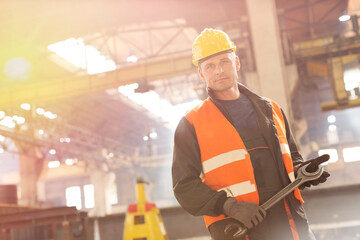 Portrait confident steel worker holding large wrench in factory - obrazy, fototapety, plakaty