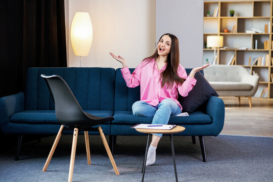 Attractive adult woman sitting on couch in living room with loft design near little table with note pad and pen. The concept of preparation for online learning