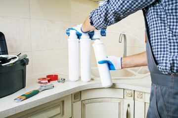  Repairman installing water filter cartridges in a kitchen. Replacing the water filter,...