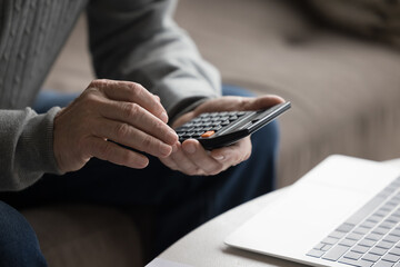 Close up crop view hands of unknown senior man count using calculator calculates expenses and incomes, manage household budget, pay taxes online in modern bank application, makes financial analysis