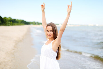 Fototapeta na wymiar Happy smiling woman in free happiness bliss on ocean beach standing with raising hands. Portrait of a multicultural female model in white summer dress enjoying nature during travel holidays vacation