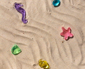 Fototapeta na wymiar Marine transparent colorful figurines or kid's toys on the beach sand. Summer sea vacation concept background. Copy space