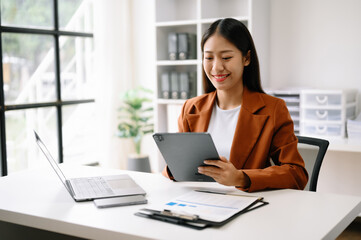 Successful Asian Businesswoman Analyzing Finance on Tablet and Laptop at Office Desk tax, report, accounting, statistics, and analytical research concept.