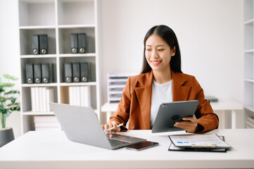Fototapeta na wymiar Successful Asian Businesswoman Analyzing Finance on Tablet and Laptop at Office Desk tax, report, accounting, statistics, and analytical research concept.