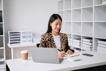 Successful Asian Businesswoman Analyzing Finance on Tablet and Laptop at Office Desk tax, report, accounting, statistics, and analytical research concept.