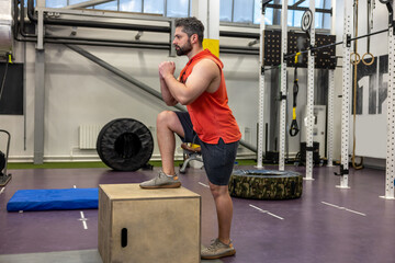 Young strong man doing workout with wooden box step up in crossfit gym.
